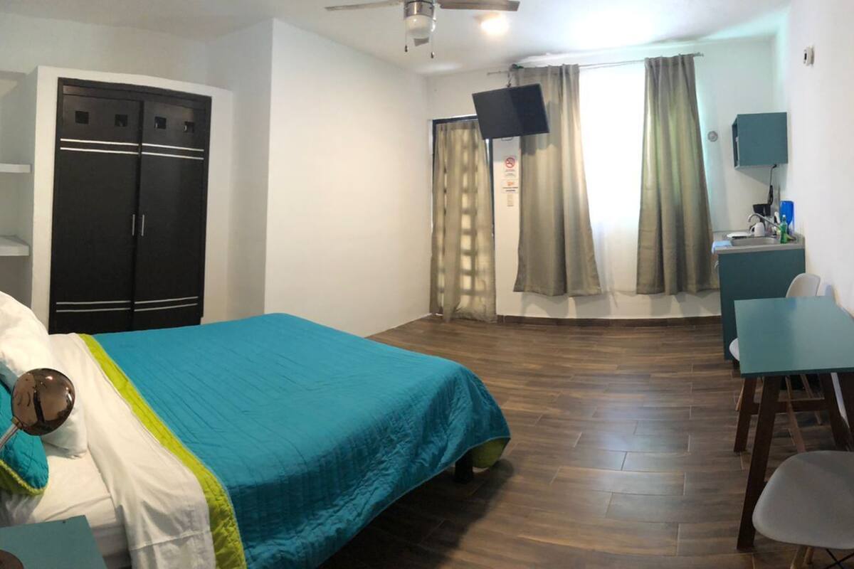 A bedroom with a bed, a desk, a chair, a wardrobe, and a television.