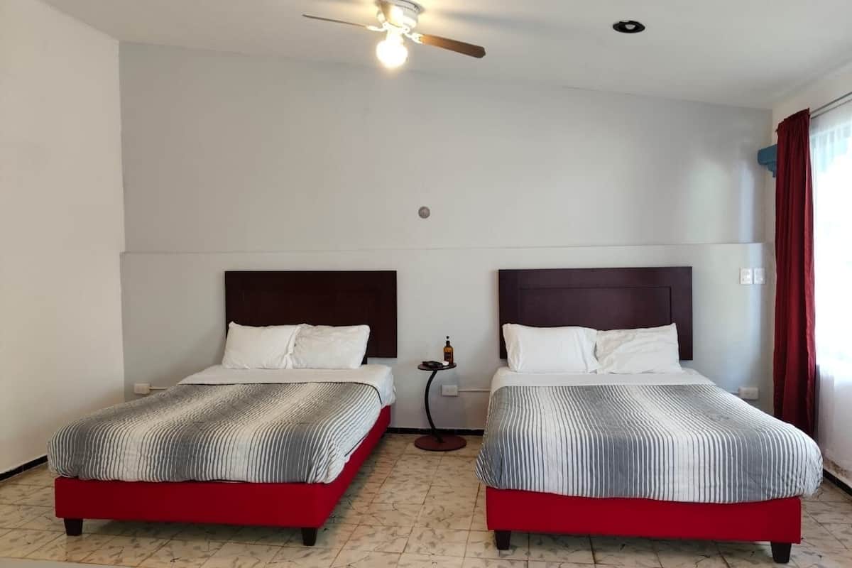 A hotel room with two beds, a ceiling fan, and a small table with a bottle.