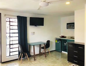 A small kitchenette with a microwave, a sink, and a cabinet. There is a table with two chairs and a ceiling fan. - Suites del Sureste (Mérida)