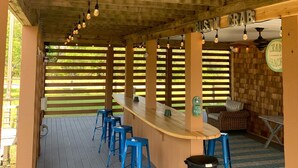 Een terras van hout met een bar, blauwe stoelen en een vuilnisbak.