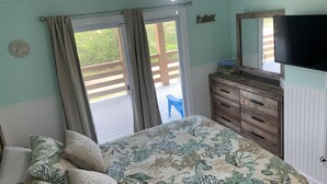 Een slaapkamer met een bed, een dressoir, een plafondventilator, een televisie en een schuifdeur die leidt naar een terras.