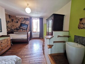 A room with a wooden floor, a bed, a dresser, a mirror, a window with curtains, and a sink.