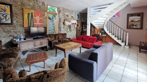A spacious living room with a stone wall, a red sofa, a blue armchair, and a wooden coffee table. - Le Patio by Interhome (Saint Malo)