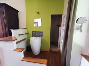 A bathroom with a white sink, green walls, wooden shelves, and a mirror.