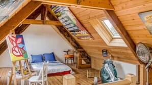 A cozy attic bedroom with a sloped ceiling, a bed with blue pillows, a small table with a chair, and a fan. - Le Patio by Interhome (Saint Malo)