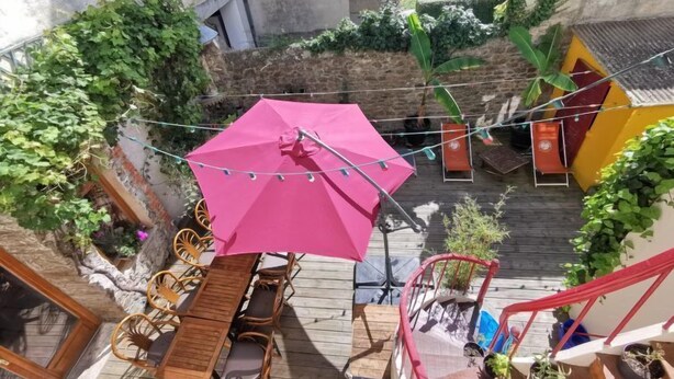 A wooden deck with a table and chairs, a pink umbrella, and string lights. - Le Patio by Interhome (Saint Malo)