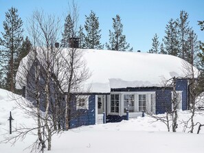A snow-covered house with a visible front door and windows, surrounded by trees.