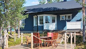 A wooden deck with a table and chairs, a covered seating area, and a house with a dark blue exterior and white trim.