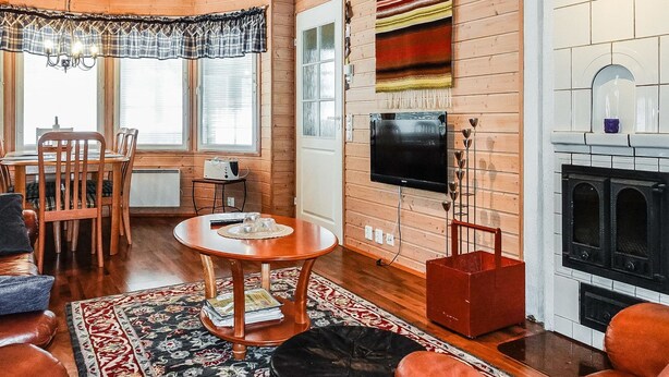 A cozy log cabin interior with a dining area, a television mounted on the wall, and a fireplace.