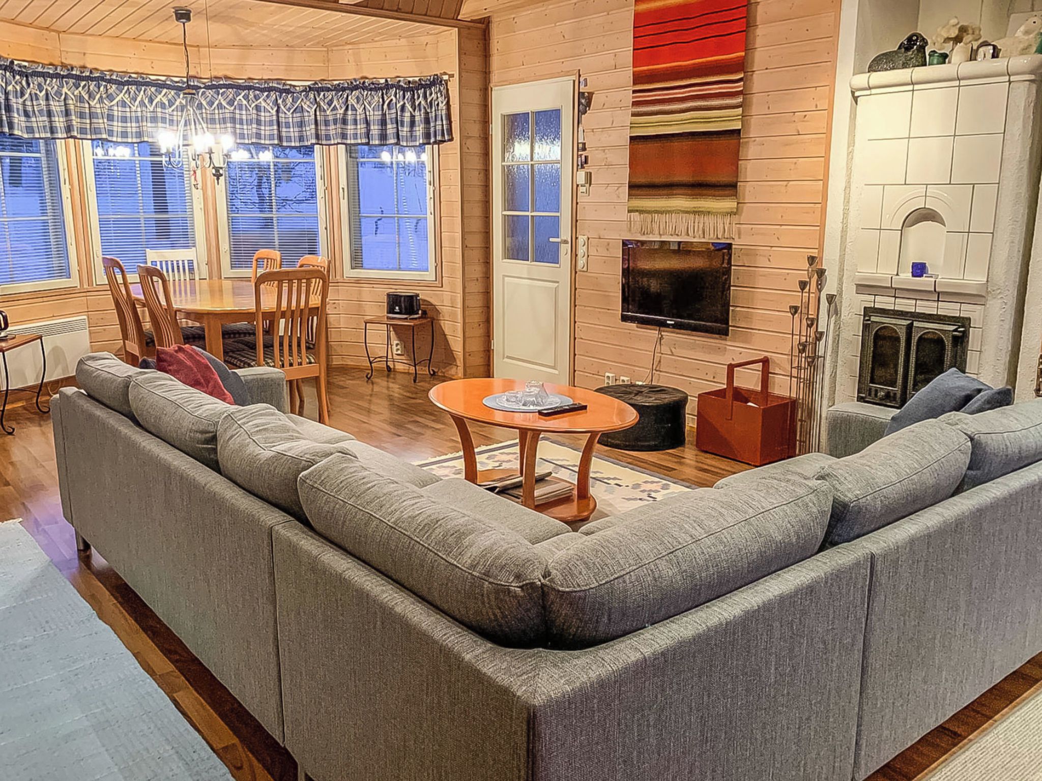 Ein gemütliches Wohnzimmer mit einem großen grauen Ecksofa, einem Holzespeisebereich mit Stühlen, einem Fernseher und einem Kamin.