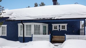 A blue house with white shutters, covered in snow, and a wooden bench in front.