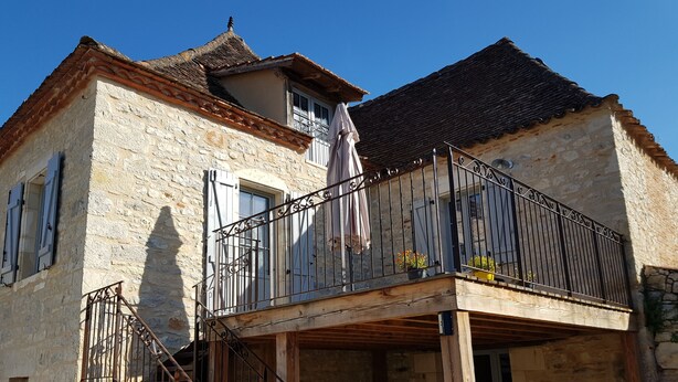 A stone building with a wooden balcony and a staircase leading to the entrance. - Gîtes Chez Antonin (Tour-de-Faure)