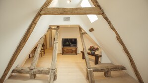 An attic room with a wooden staircase, a television, and a small table with flowers. - Gîtes Chez Antonin (Tour-de-Faure)