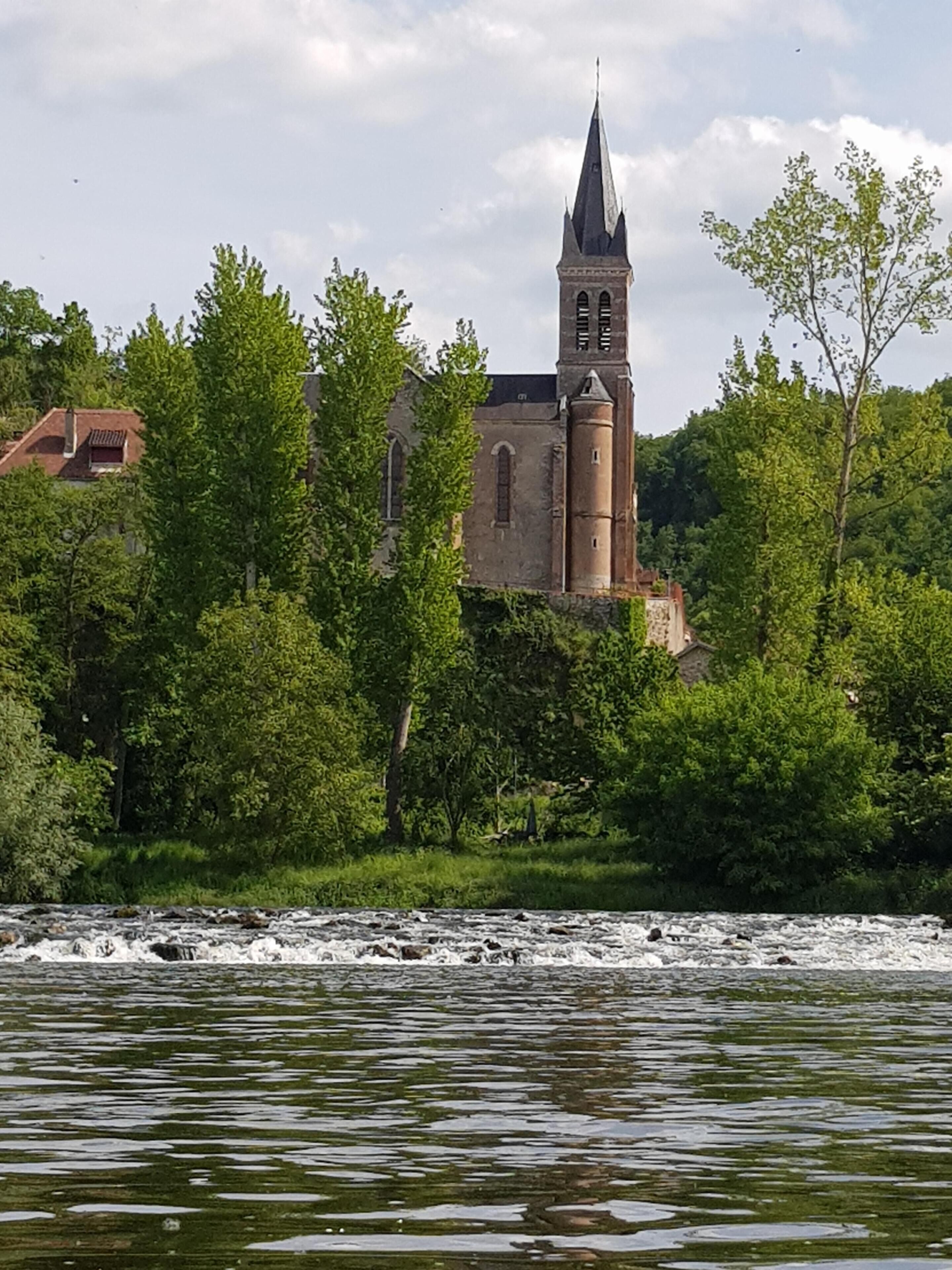 A historic church with a tall tower and a river in the foreground.