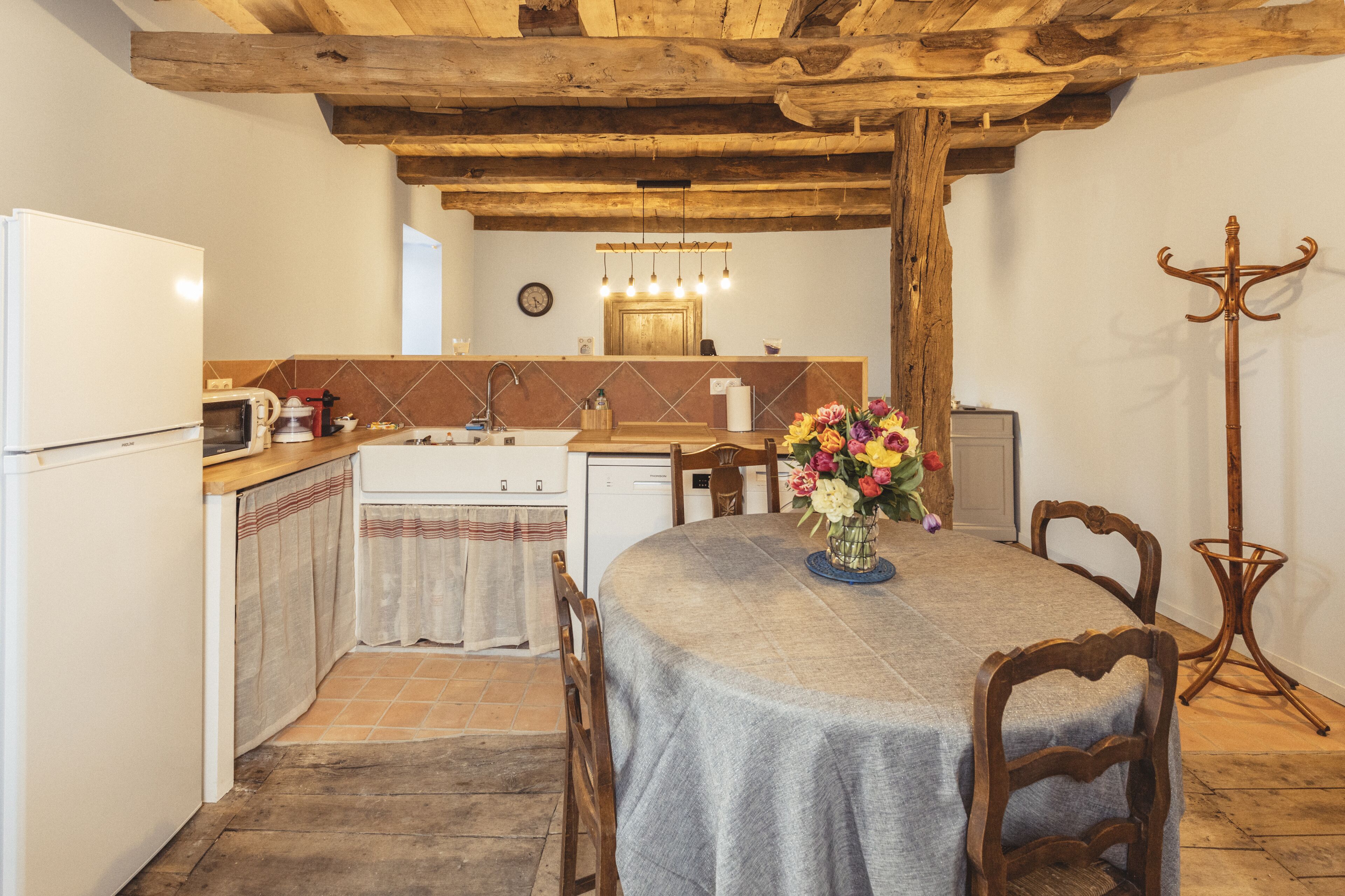 A rustic kitchen with a wooden ceiling, a dining table with chairs, a sink, and a coat rack.
