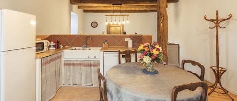 A rustic kitchen with a wooden ceiling, a dining table with chairs, a sink, and a coat rack.