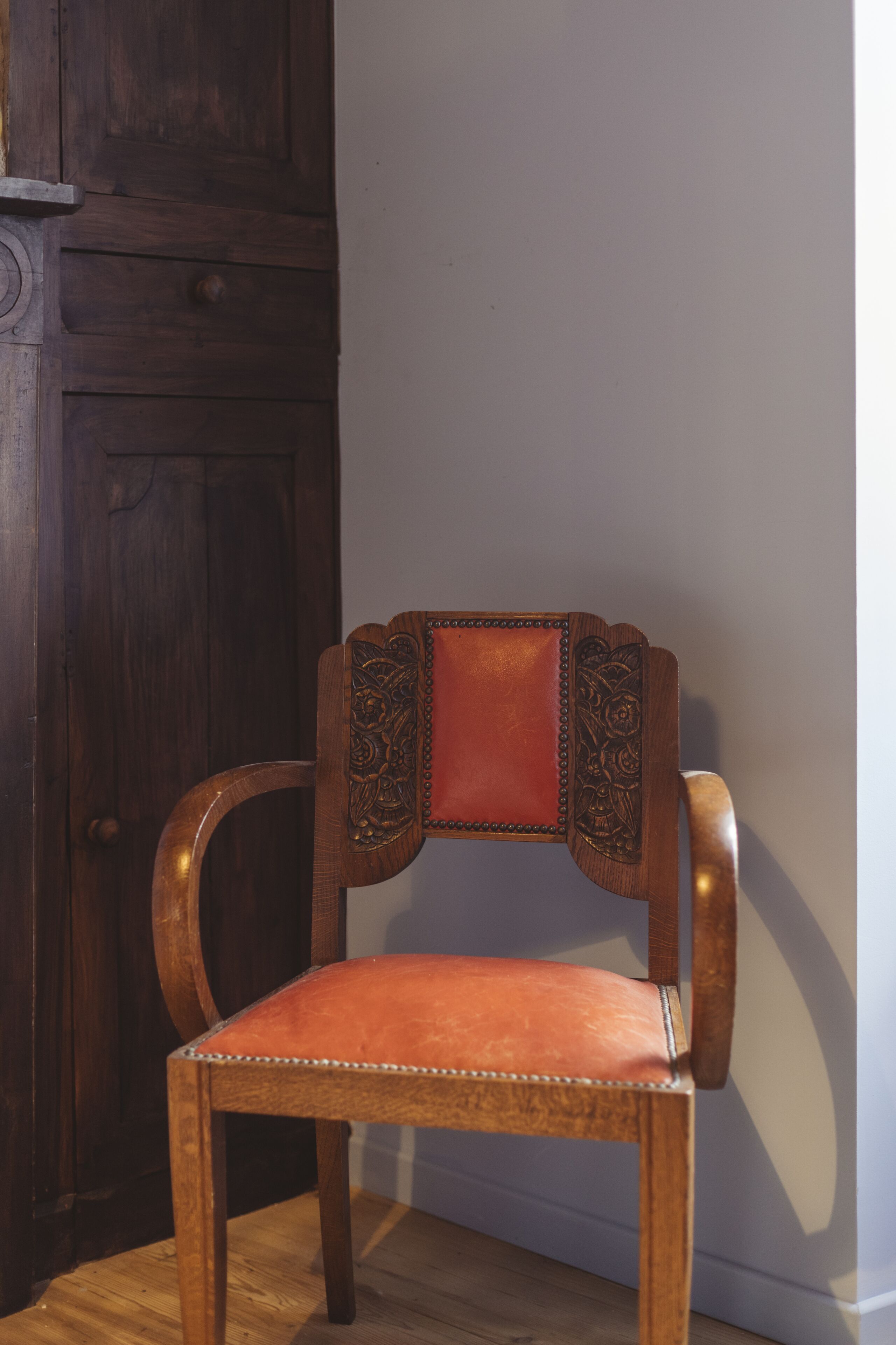 A wooden chair with a cushioned seat and backrest, positioned against a wall.
