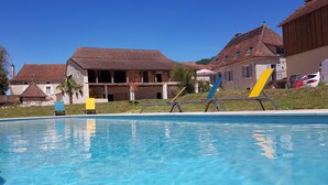 A swimming pool with clear blue water, surrounded by stone buildings with red-tiled roofs. - Gîtes Chez Antonin (Tour-de-Faure)
