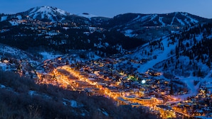 Un paese montano imbiancato dalla neve al crepuscolo, con edifici illuminati e strade tortuose.