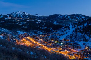A snow-covered mountain town at dusk with illuminated buildings and winding roads.