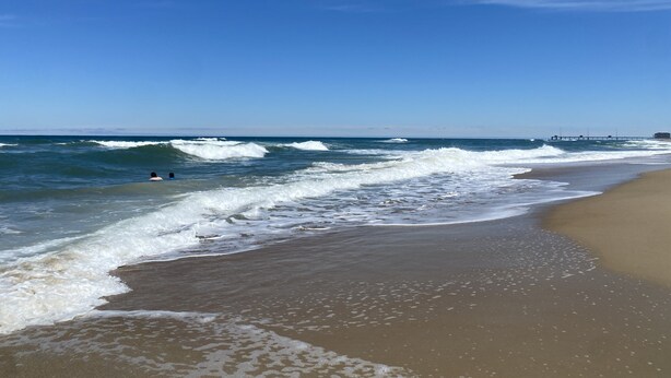 A beach with waves, a pier, and a clear sky.