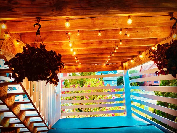Una escalera de madera que termina en un banco azul, conduciendo a una cerca blanca con plantas de colores.