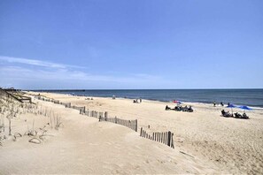 Une plage de sable bordée d’une clôture en bois et d’une jetée qui s’avance dans l’eau.