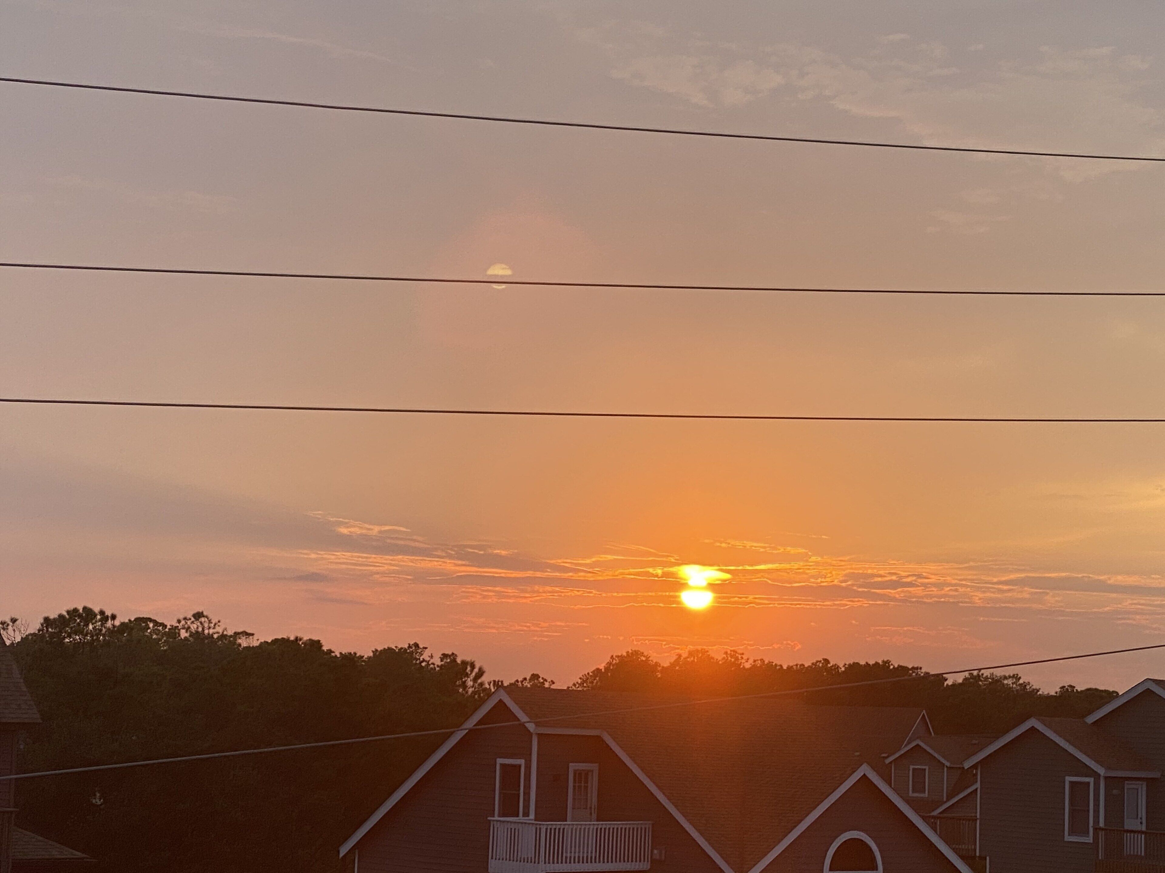 A sunset over a residential area with houses and power lines.