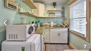 A compact kitchen with white cabinets, a built-in washing machine, and a window with blinds.