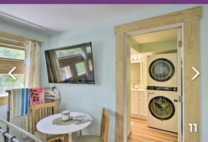 Une pièce comprenant une table à manger, des chaises, un téléviseur fixé au mur et un lave-linge dans la pièce adjacente.