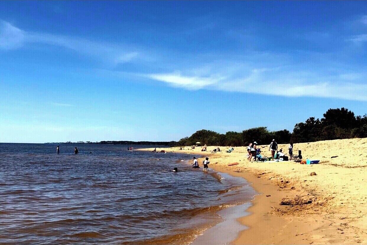 A beach with people swimming and relaxing on the sand.