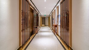A long, narrow hallway with a polished floor, wooden paneling on the walls, and a central exit sign. - Bo Yi Hotel (Guangzhou)