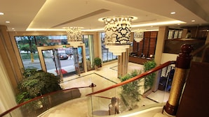 A modern hotel lobby with a glass staircase, elegant chandeliers, and a view of the street outside. - Bo Yi Hotel (Guangzhou)