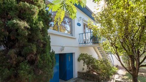 A two-story building with a blue door and balcony, surrounded by greenery and trees. - Les Mâts by Interhome (Saint Palais sur mer)
