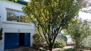 A modern house with a blue garage door, a staircase leading to a balcony, and a tree in the front yard. - Les Mâts by Interhome (Saint Palais sur mer)