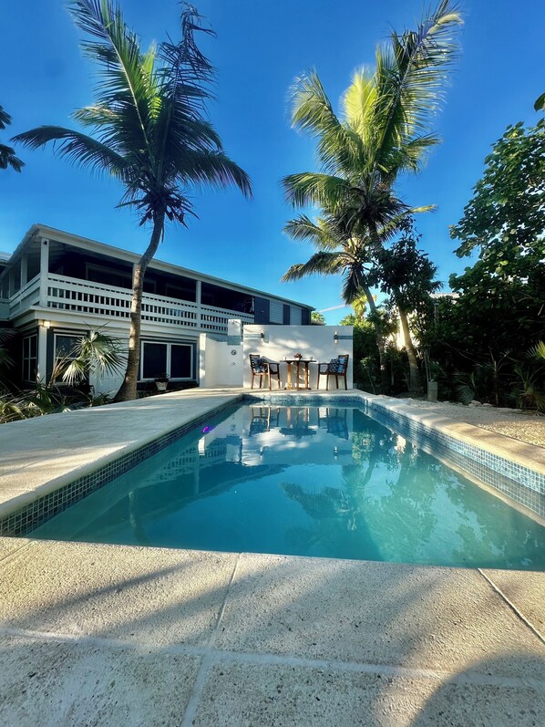A swimming pool with a tiled edge, surrounded by palm trees and a building with a balcony.
