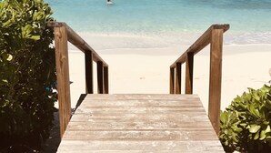Un sendero de madera que conduce a una playa con agua turquesa cristalina y un barco a lo lejos.