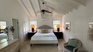 Un dormitorio amplio con una cama grande, un ventilador de techo y vistas al exterior a través de las ventanas.