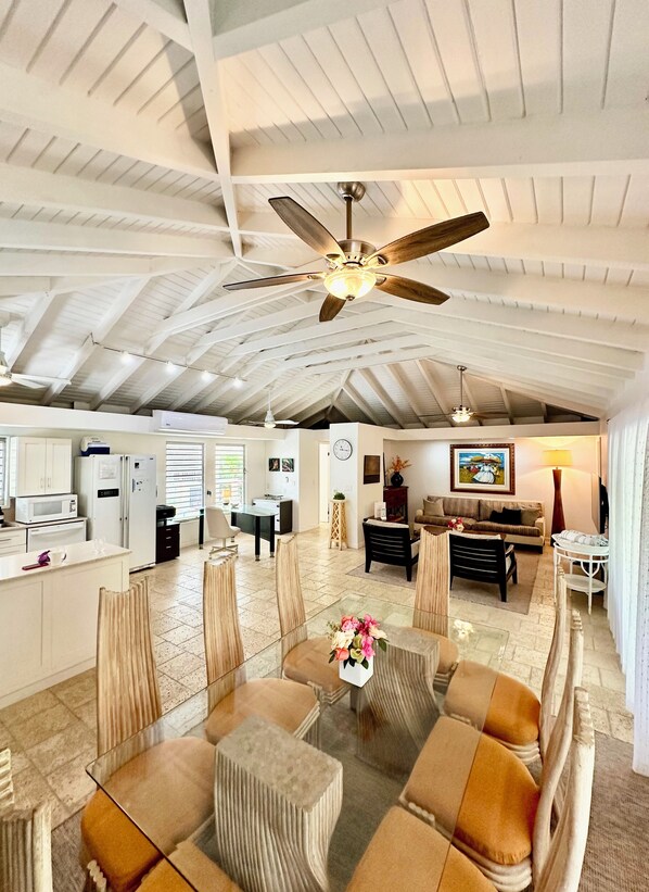 A spacious living area with a high ceiling, a ceiling fan, and a dining area with a table and chairs.