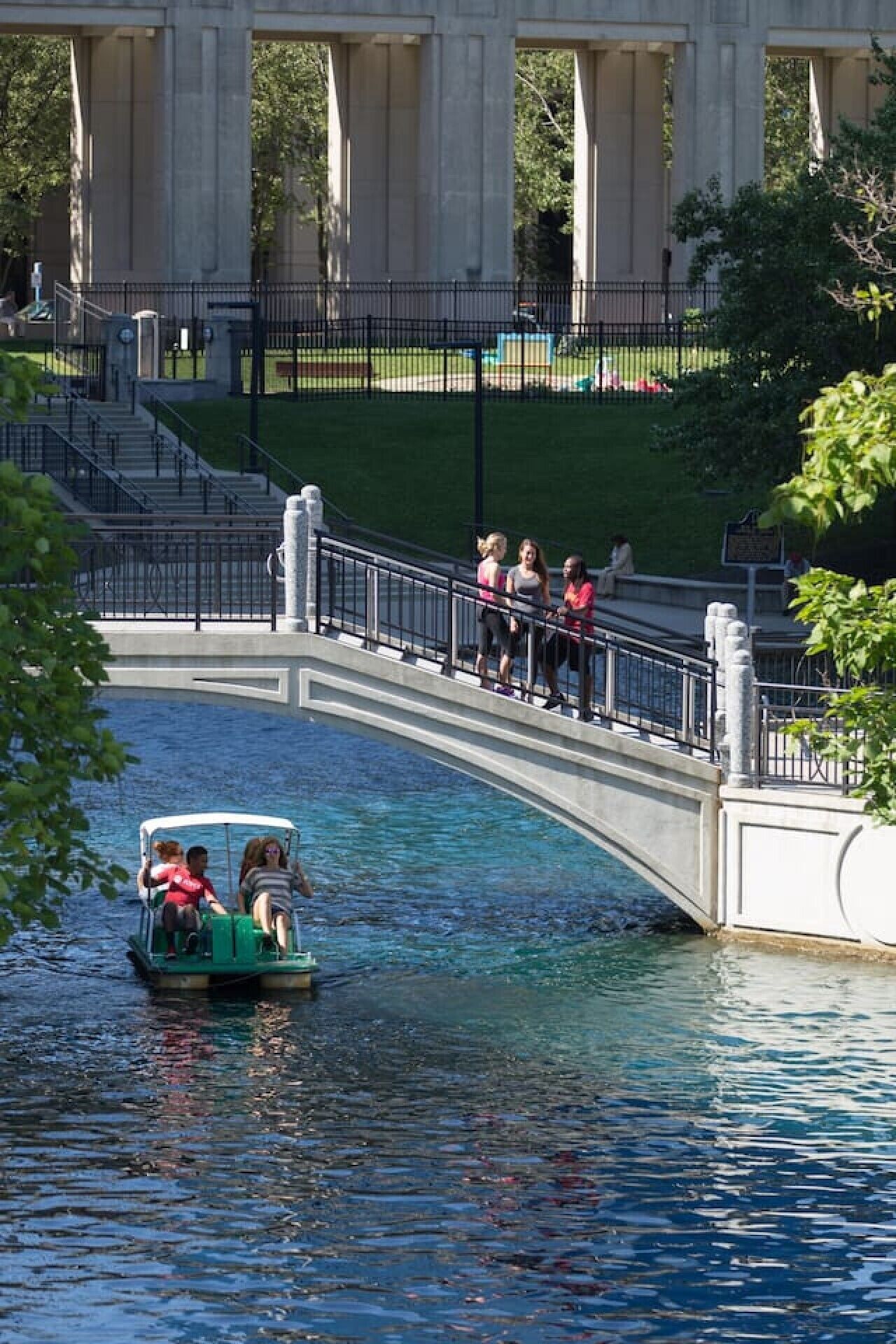 Ein Kanal mit einem grünen Boot, einer Brücke und Personen auf der Brücke.