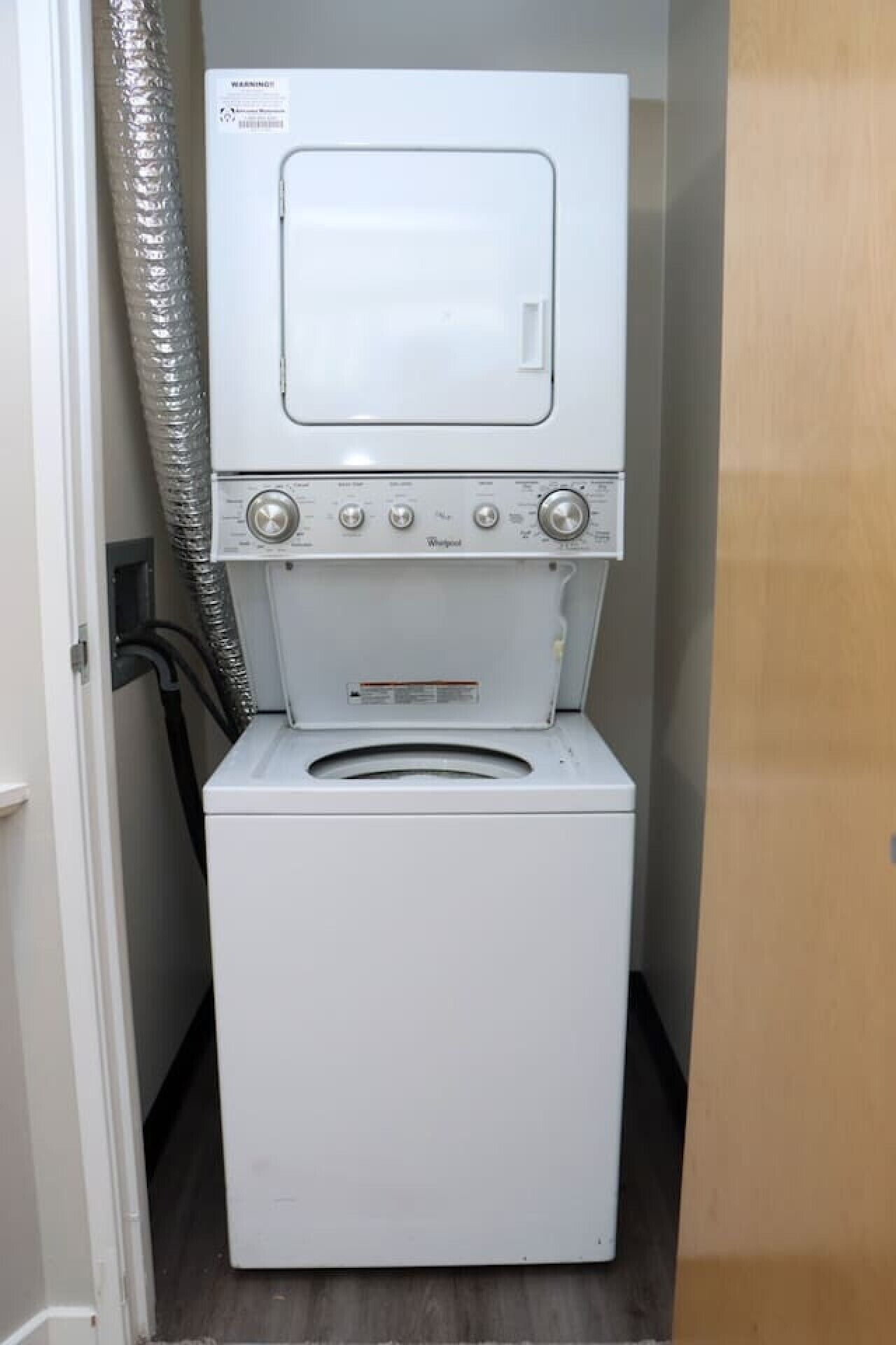 A compact washer and dryer unit in a small laundry room with a wooden door and a vent hose.