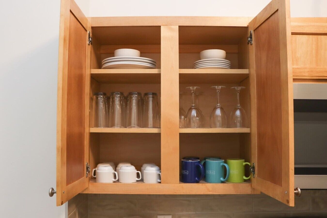 A wooden cabinet with shelves containing plates, glasses, and mugs.