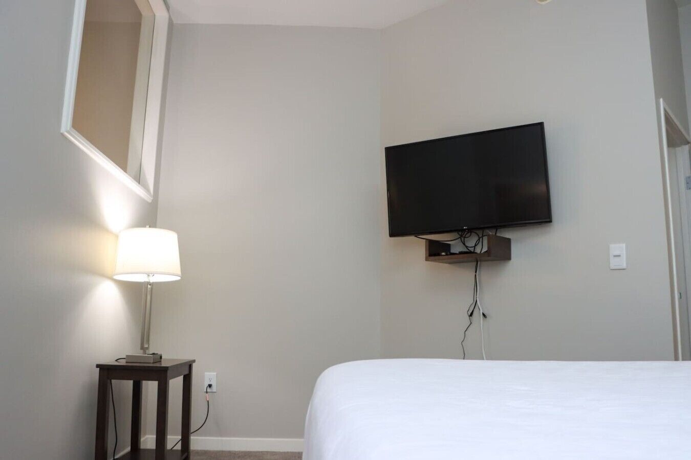 Une chambre d’hôtel comprenant un lit, une table de chevet avec une lampe, un téléviseur à écran plat fixé au mur et une prise de courant.