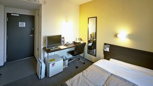 Habitación de hotel con cama, escritorio con computadora, silla, refrigerador pequeño y espejo en la pared.