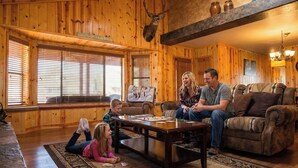 A wooden interior with a fireplace, a couch, a coffee table, and a deer head mounted on the wall. - Cozy and lakefront cabin on Rainbow lake, large fenced deck and 2 grills!!! (Pinetop-Lakeside)