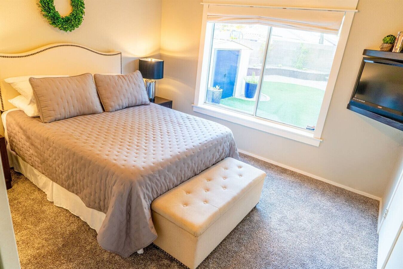A bedroom with a bed, a nightstand, a lamp, a window, and a TV.