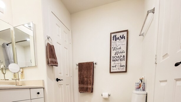 Une salle de bain avec un plancher en bois, des meubles blancs, des toilettes et un miroir.
