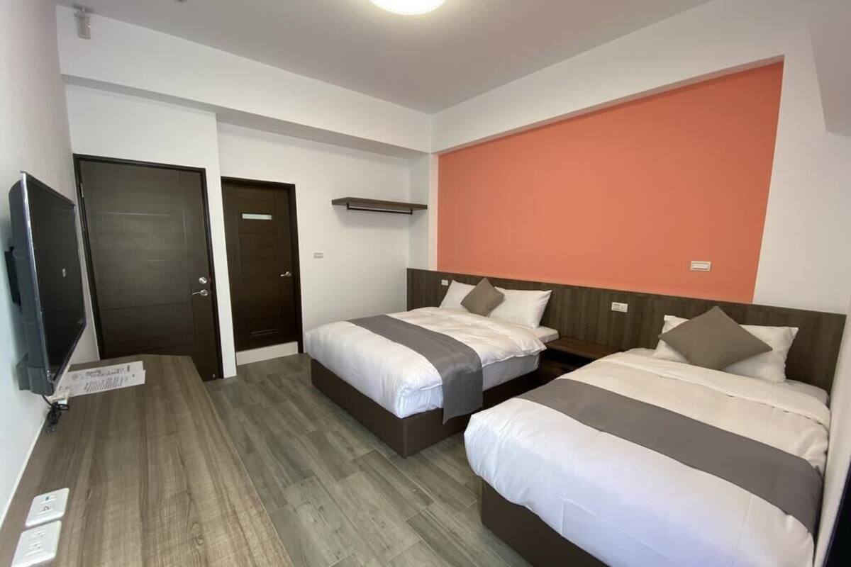 A hotel room with two beds, a television, and a wooden floor.