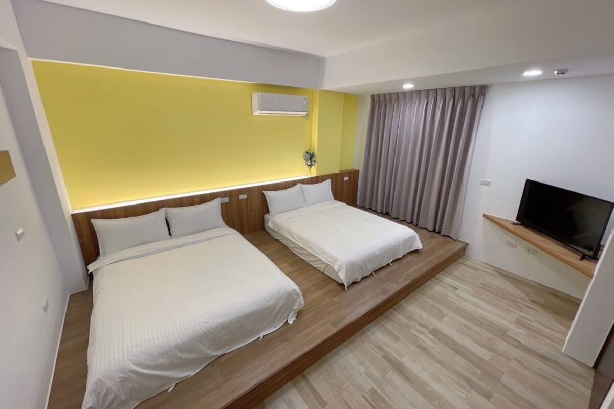 A hotel room with two beds, a TV, and a yellow accent wall.