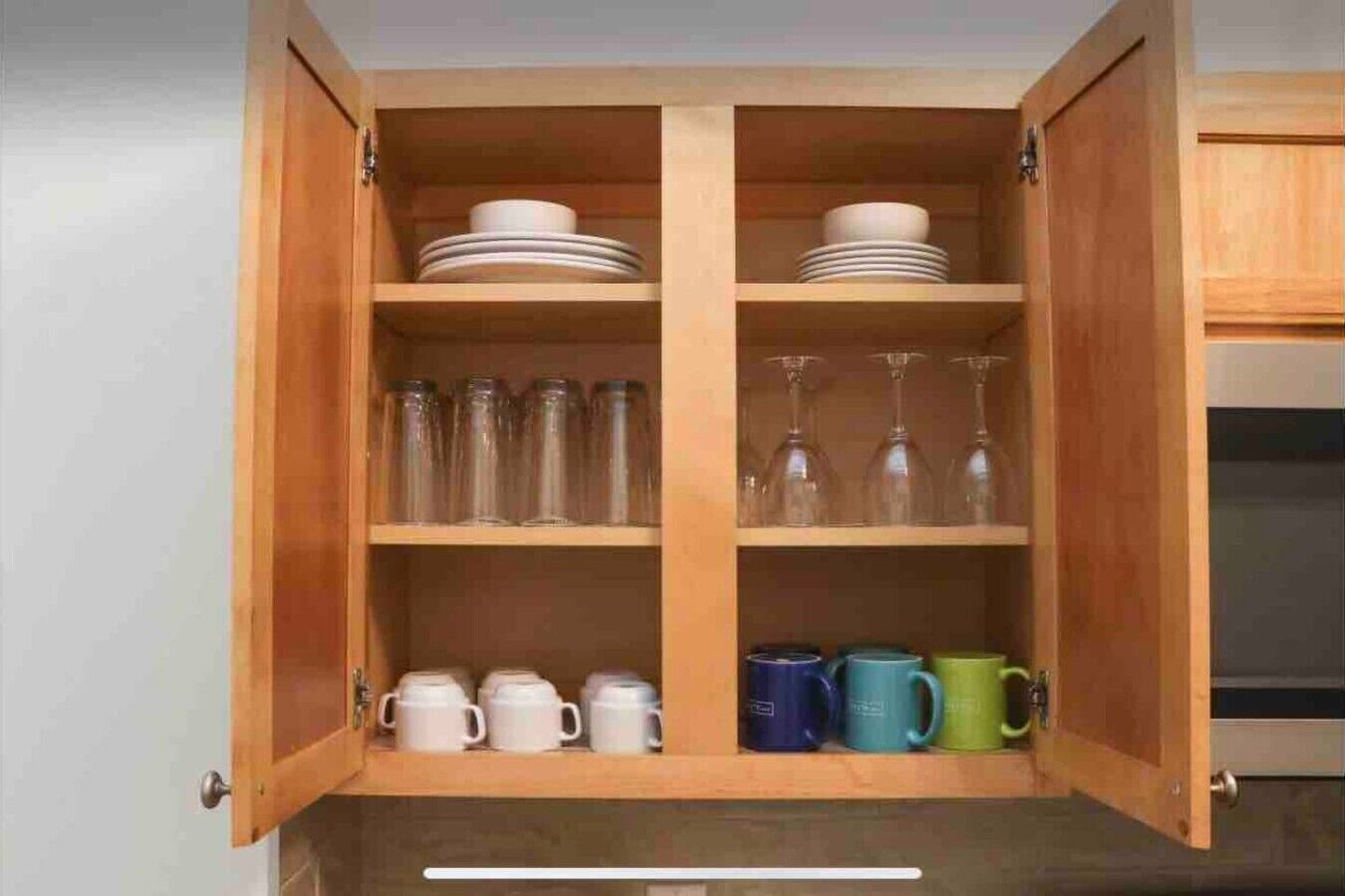 A wooden cabinet with shelves containing plates, glassware, and mugs.